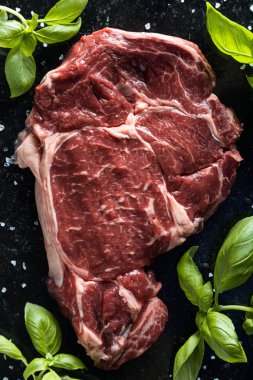 Taze biftek servis ile baharat, domates ve fesleğen mermer zemin üzerine yapraklar. Bir mutfak yemek pişmemiş biftek. Lezzetli, baharatlı, sulu et kopya alanı closeup ile