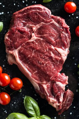 Taze biftek servis ile baharat, domates ve fesleğen mermer zemin üzerine yapraklar. Bir mutfak yemek pişmemiş biftek. Lezzetli, baharatlı, sulu et kopya alanı closeup ile