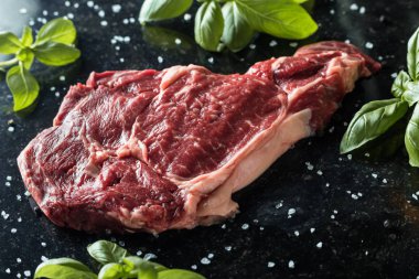 Taze biftek servis ile baharat, domates ve fesleğen mermer zemin üzerine yapraklar. Bir mutfak yemek pişmemiş biftek. Lezzetli, baharatlı, sulu et kopya alanı closeup ile