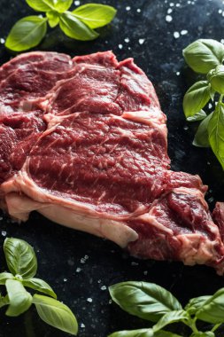 Taze biftek servis ile baharat, domates ve fesleğen mermer zemin üzerine yapraklar. Bir mutfak yemek pişmemiş biftek. Lezzetli, baharatlı, sulu et kopya alanı closeup ile