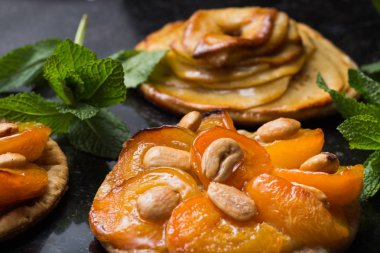 Kayısı ve elma tart. Karanlık mermer zemin üzerine meyve ile geleneksel Fransız pasta. Bir şekilde dekore edilmiş badem ve nane yaprakları. Kopyalama alanı closeup ile lezzetli tatlı