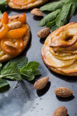 Kayısı ve elma tart. Karanlık mermer zemin üzerine meyve ile geleneksel Fransız pasta. Bir şekilde dekore edilmiş badem ve nane yaprakları. Kopyalama alanı closeup ile lezzetli tatlı