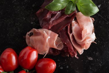 Jambon karışımı. Jambon. Geleneksel İtalyan ve İspanyol Tuzlama, Sigara, otlar ve karanlık taş zemin üzerine domates kuru tedavi çanak - jamon Serrano ve prosciutto crudo dilimlenmiş. Uzay kopyalayın. Portre