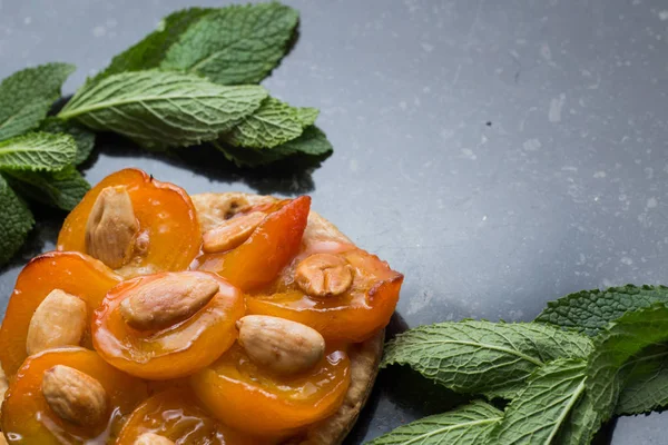 Tart with apricot. Traditional french pie with fruits on dark marble background. Decorated almonds and mint leafs. Delicious dessert with copy space closeup — Stock Photo, Image