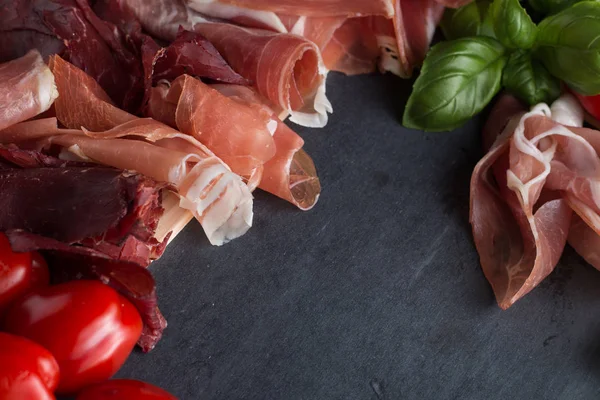 Jambon karışımı. Jambon. Geleneksel İtalyan ve İspanyol Tuzlama, Sigara, otlar ve karanlık taş zemin üzerine domates kuru tedavi çanak - jamon Serrano ve prosciutto crudo dilimlenmiş. Uzay kopyalayın. Portre