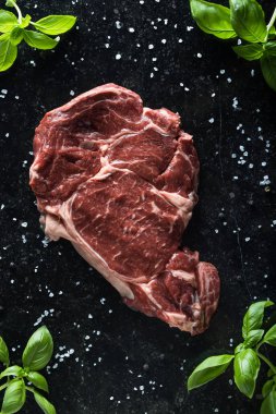 Taze biftek servis ile baharat, domates ve fesleğen mermer zemin üzerine yapraklar. Bir mutfak yemek pişmemiş biftek. Lezzetli, baharatlı, sulu et kopya alanı closeup ile