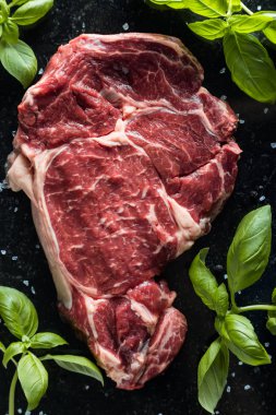 Taze biftek servis ile baharat, domates ve fesleğen mermer zemin üzerine yapraklar. Bir mutfak yemek pişmemiş biftek. Lezzetli, baharatlı, sulu et kopya alanı closeup ile