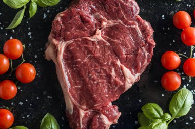 Taze biftek servis ile baharat, domates ve fesleğen mermer zemin üzerine yapraklar. Bir mutfak yemek pişmemiş biftek. Lezzetli, baharatlı, sulu et kopya alanı closeup ile