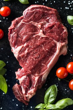 Taze biftek servis ile baharat, domates ve fesleğen mermer zemin üzerine yapraklar. Bir mutfak yemek pişmemiş biftek. Lezzetli, baharatlı, sulu et kopya alanı closeup ile