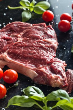 Taze biftek servis ile baharat, domates ve fesleğen mermer zemin üzerine yapraklar. Bir mutfak yemek pişmemiş biftek. Lezzetli, baharatlı, sulu et kopya alanı closeup ile