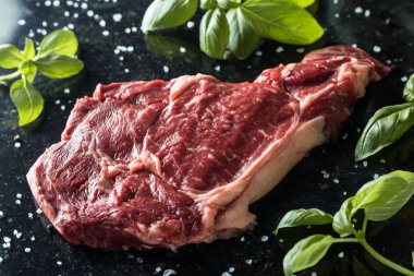 Taze biftek servis ile baharat, domates ve fesleğen mermer zemin üzerine yapraklar. Bir mutfak yemek pişmemiş biftek. Lezzetli, baharatlı, sulu et kopya alanı closeup ile