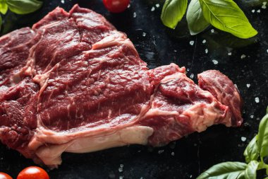 Taze biftek servis ile baharat, domates ve fesleğen mermer zemin üzerine yapraklar. Bir mutfak yemek pişmemiş biftek. Lezzetli, baharatlı, sulu et kopya alanı closeup ile