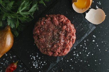 Çiğ biftek. Sığır eti çiğ et baharat, ot ve yumurta sarısı ile kıyılmış. Taze, baharatlı, lezzetli, gurme yemek ile kopya alanı, koyu arka plan üzerinde yakın çekim. Üstten Görünüm.