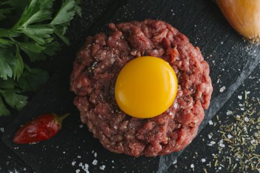 Çiğ biftek. Sığır eti çiğ et baharat, ot ve yumurta sarısı ile kıyılmış. Taze, baharatlı, lezzetli, gurme yemek ile kopya alanı, koyu arka plan üzerinde yakın çekim. Üstten Görünüm.