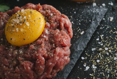 Çiğ biftek. Sığır eti çiğ et baharat, ot ve yumurta sarısı ile kıyılmış. Taze, baharatlı, lezzetli, gurme yemek ile kopya alanı, koyu arka plan üzerinde yakın çekim.