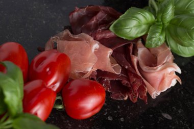 Jambon karışımı. Jambon. Geleneksel İtalyan ve İspanyol Tuzlama, Sigara, otlar ve karanlık taş zemin üzerine domates kuru tedavi çanak - jamon Serrano ve prosciutto crudo dilimlenmiş. Uzay kopyalayın. Portre
