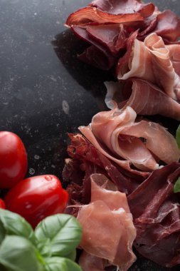 Jambon karışımı. Jambon. Geleneksel İtalyan ve İspanyol Tuzlama, Sigara, otlar ve karanlık taş zemin üzerine domates kuru tedavi çanak - jamon Serrano ve prosciutto crudo dilimlenmiş. Uzay kopyalayın. Portre