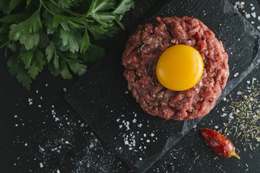 Çiğ biftek. Sığır eti çiğ et baharat, ot ve yumurta sarısı ile kıyılmış. Taze, baharatlı, lezzetli, gurme yemek ile kopya alanı, koyu arka plan üzerinde yakın çekim. Üstten Görünüm.