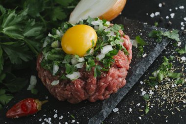 Çiğ biftek. Sığır eti çiğ et baharat, ot ve yumurta sarısı ile kıyılmış. Taze, baharatlı, lezzetli, gurme yemek ile kopya alanı, koyu arka plan üzerinde yakın çekim.