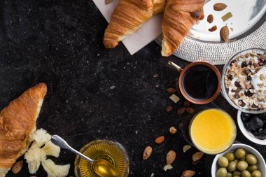 Kahvaltı çeşitli yoğurt, granola, kahve, meyve suyu, kruvasan, zeytin. Meze sabah yemekleri ile karıştırın. Koyu arka plan üzerinde sağlıklı, taze, lezzetli yemek. Üstten Görünüm. Kopya alanı