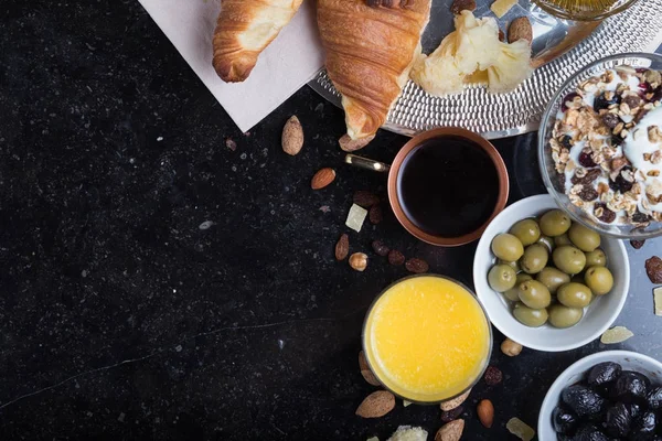 Colazione assortiti yogurt, muesli, caffè, succo di frutta, croissant, olive. Miscela antipasto con piatti del mattino. Cibo sano, fresco e delizioso su sfondo scuro. Vista dall'alto. Copia spazio — Foto Stock