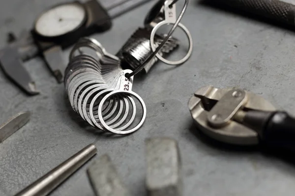 Conjunto de ferramentas de joalharia. Local de trabalho de jóias em fundo de metal. Dimensionamento do dedo para anéis, bússola de feixe, pinça, garras — Fotografia de Stock
