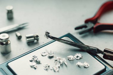 Takı araçları. Takı. Goldsmith işyeri, çalışma alanında açık renkli. El tekne. Atölye. Üretim. Ağırlık pullarla granül metal gümüş ve platin. Portre. Tonda