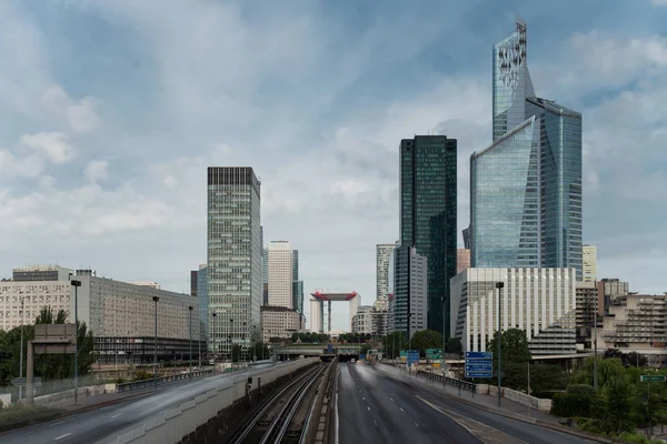 Moderní budovy a dynamické pouliční provoz v pařížské obchodní čtvrti La Défense. Panoráma města s skleněnou fasádou mrakodrapy na zamračený den. Ekonomika, finance, silniční síť a městské dopravní koncepce — Stock fotografie