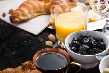 Kahvaltı çeşitli yoğurt, granola, kahve, meyve suyu, kruvasan, zeytin. Meze sabah yemekleri ile karıştırın. Koyu arka plan üzerinde sağlıklı, taze, lezzetli yemek