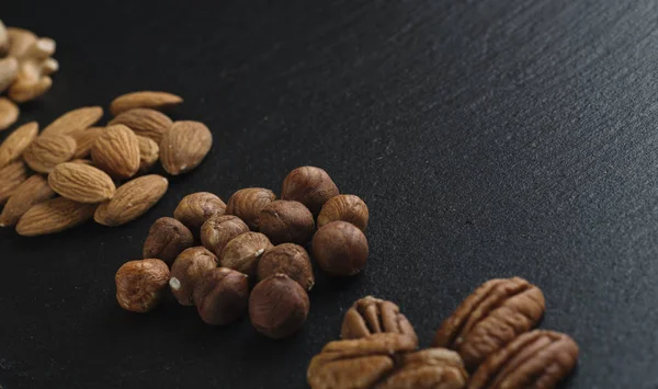 Variety of mixed nuts - almond, hazelnuts and cashew - on the dark slate background with copy space. Top view. Toned