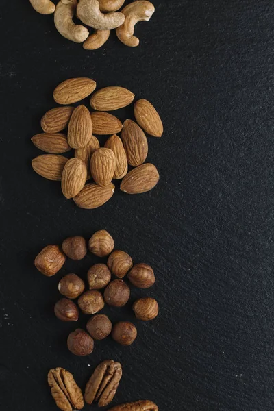 Variety of mixed nuts - almond, hazelnuts and cashew - on the dark slate background with copy space. Top view. Toned