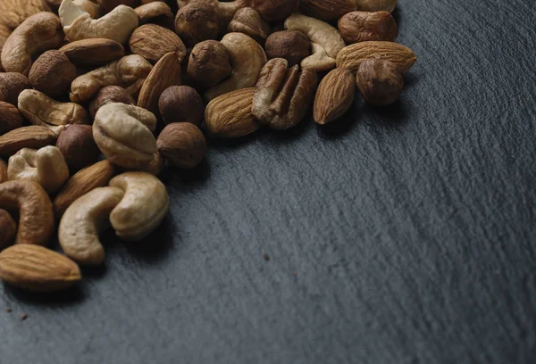 Mängd blandade nötter - mandel, hasselnötter och cashew - på mörk skiffer bakgrunden med kopia utrymme. Ovanifrån. Tonas — Stockfoto