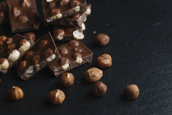 Chocolate bar pieces and nuts on dark slate background with copy space. Chocolate background. Top view. Toned