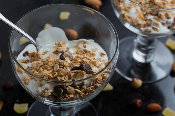 Granola con yogurt, noci e frutta in ciotola di vetro su fondo scuro. Delizioso dolce dolce sano per colazione. Cereali, muesli. Copia spazio, primo piano — Foto Stock