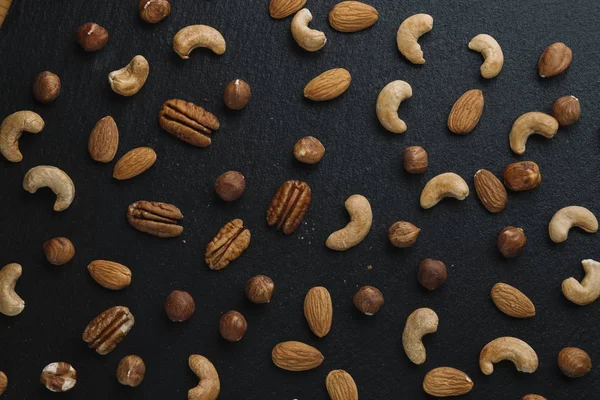 Variety of mixed nuts - almond, hazelnuts and cashew - on the dark slate background with copy space. Top view. Toned