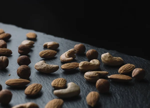 Variety of mixed nuts - almond, hazelnuts and cashew - on the dark slate background with copy space. Top view. Toned