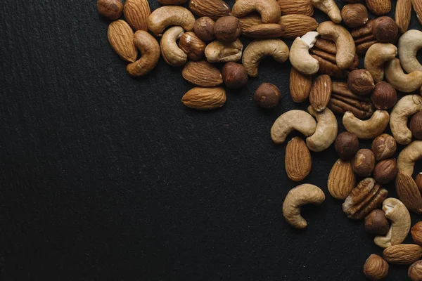 Různé namíchané oříšky - mandle, lískové ořechy a kešu - na tmavém pozadí břidlice s kopie prostoru. Pohled shora. Tónovaný — Stock fotografie