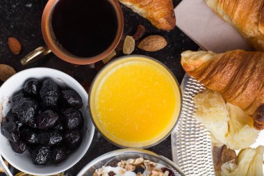 Kahvaltı çeşitli yoğurt, granola, kahve, meyve suyu, kruvasan, zeytin. Meze sabah yemekleri ile karıştırın. Koyu arka plan üzerinde sağlıklı, taze, lezzetli yemek