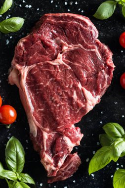 Taze biftek servis ile baharat, domates ve fesleğen mermer zemin üzerine yapraklar. Bir mutfak yemek pişmemiş biftek. Lezzetli, baharatlı, sulu et kopya alanı closeup ile