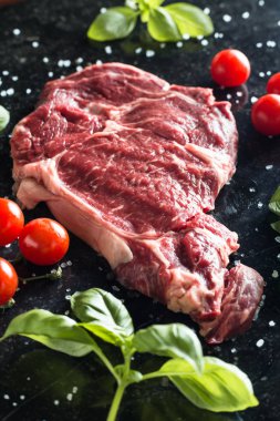Taze biftek servis ile baharat, domates ve fesleğen mermer zemin üzerine yapraklar. Bir mutfak yemek pişmemiş biftek. Lezzetli, baharatlı, sulu et kopya alanı closeup ile
