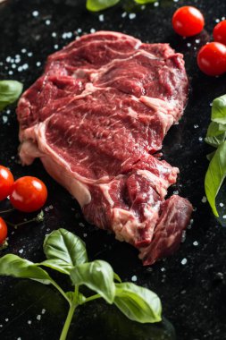 Taze biftek servis ile baharat, domates ve fesleğen mermer zemin üzerine yapraklar. Bir mutfak yemek pişmemiş biftek. Lezzetli, baharatlı, sulu et kopya alanı closeup ile