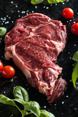 Taze biftek servis ile baharat, domates ve fesleğen mermer zemin üzerine yapraklar. Bir mutfak yemek pişmemiş biftek. Lezzetli, baharatlı, sulu et kopya alanı closeup ile