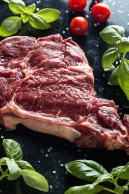 Taze biftek servis ile baharat, domates ve fesleğen mermer zemin üzerine yapraklar. Bir mutfak yemek pişmemiş biftek. Lezzetli, baharatlı, sulu et kopya alanı closeup ile
