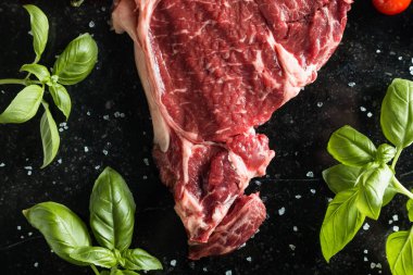 Taze biftek servis ile baharat, domates ve fesleğen mermer zemin üzerine yapraklar. Bir mutfak yemek pişmemiş biftek. Lezzetli, baharatlı, sulu et kopya alanı closeup ile