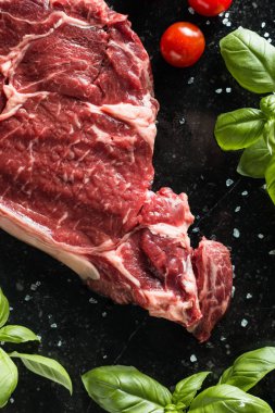 Taze biftek servis ile baharat, domates ve fesleğen mermer zemin üzerine yapraklar. Bir mutfak yemek pişmemiş biftek. Lezzetli, baharatlı, sulu et kopya alanı closeup ile