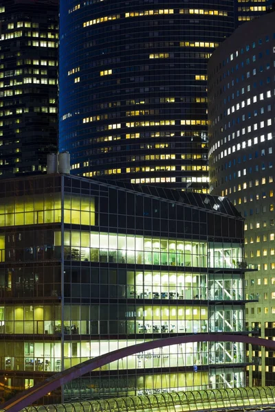 Modern buildings in Paris business district La Defense. Night cityscape with glass facades of skyscrapers. City lights, urban architecture, contemporary city life. Economy, financial activity concept
