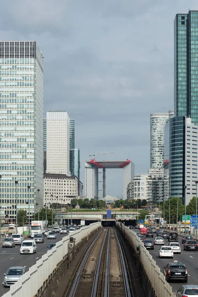 Moderní budovy a dynamické pouliční provoz v pařížské obchodní čtvrti La Défense. Panoráma města s skleněnou fasádou mrakodrapy na zamračený den. Ekonomika, finance, silniční síť a městské dopravní koncepce — Stock fotografie