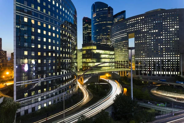 Arranha-céus no distrito empresarial de Paris La Defense. Cidade noturna europeia com tráfego de rua dinâmico, luzes de carro e fachadas de vidro de edifícios modernos. Economia, finanças, conceito de transporte. Tonificado — Fotografia de Stock