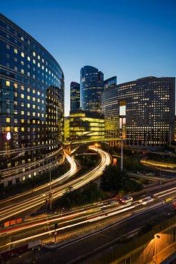 Paris iş içinde gökdelenler La Defense bölge. Avrupa gece cityscape dinamik sokak trafik, araba ışıklar ve modern binalar cam cephe ile. Ekonomi, Maliye, Ulaştırma kavramı. Tonda