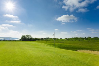 Parlak güneşli bir günde bir yeşil golf sahası, delik ve bayrak görünümünü. Spor, sakin ol, rekreasyon ve eğlence kavramı. Güneş ışınları, yaz yatay